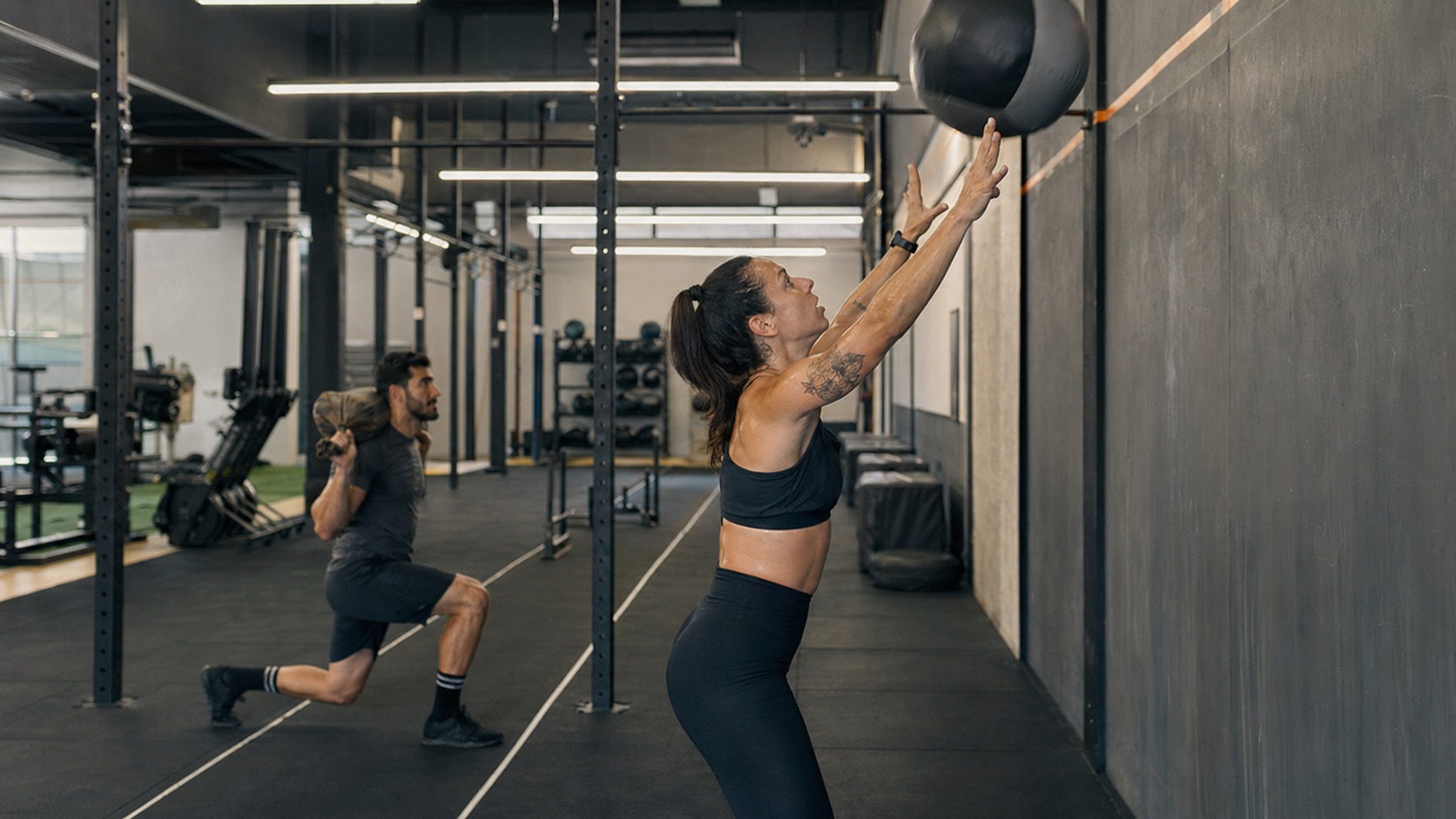 Atletas treinando wall balls e sandbag lunges em uma academia funcional para HYROX